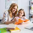 © LIGHTFIELD STUDIOS - Selective focus of smiling mother and kid looking at notebook near laptop and books on table