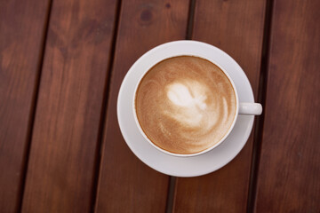 Cup of cappuccino on the wooden background. Beautiful brown foam, white ceramic cup, place for text