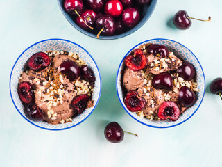 Two chocolate ice cream sundae with cherries, almond and chocolate sprinkles on green turquoise background. Top view