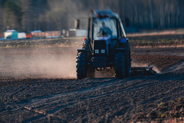 Tractor with a disc harrow system harrows the cultivated farm field, process of harrowing and preparing the soil, tractor seeding crops at field on sunset, agriculture concept, harrow machine at work