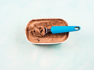 Ice cream scoop in chocolate ice cream tub on green turquoise background. Closeup