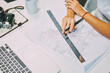© BullRun - Cropped view of young woman sitting at desktop with building blueprint working on developing architectural project.Top view of table with engineering draft on paper sketch and vintage camera