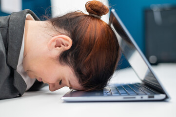 Exhausted Frustrated business woman put her head down on a notebook sitting at a desk. A female employee worked overtime and fell asleep at a computer in the office. Hard worker.