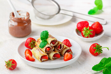 Wall Mural - Rolls with chocolate and nut filling (Nutella), fresh strawberry berries, powdered sugar and mint. Delicious gourmet Breakfast. Selective focus