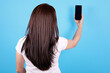 © Sviatoslav Kovtun - Brunette girl with long hair using mobile phone, make selfie, view from behind. Isolated on blue background.