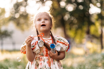 A girl with Down syndrome blows bubbles. The daily life of a child with disabilities. Chromosomal genetic disorder in a child.