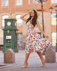 Young woman in colorful dress walking city street on a sunny summer day. Full length portrait. Elegant lady with long wavy hair. Girl in sunglasses