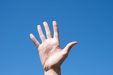 Wall Mural - Gesture closeup of a woman's hand showing five fingers, isolated against a blue sky, sign language symbol number five