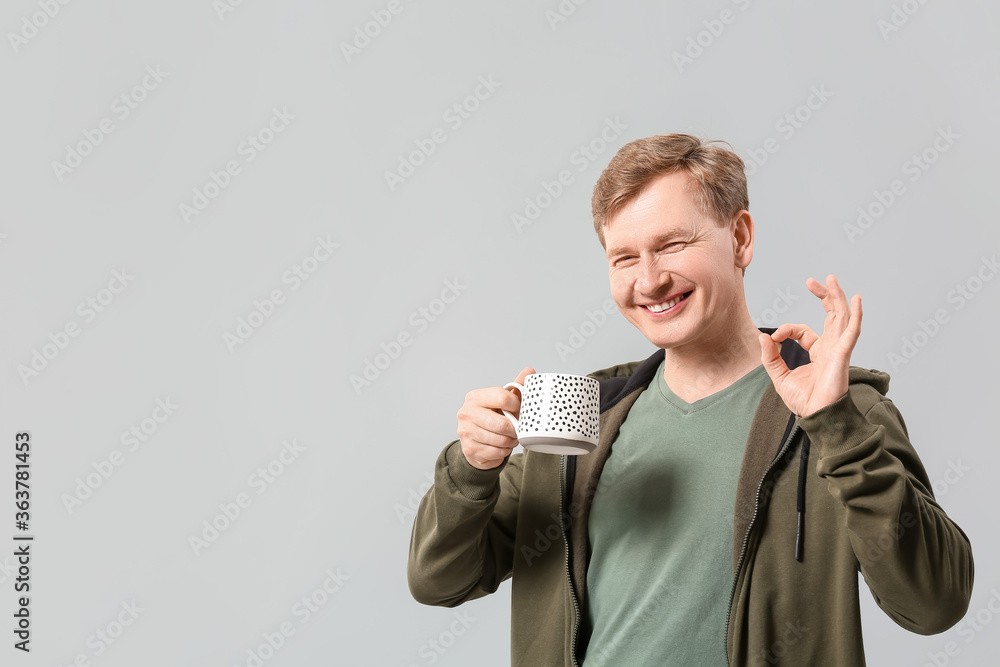 Handsome man with cup of tea showing OK on grey background