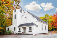 White Country Baptist Church Surrounded By Beautiful Foliage Colors In New England Autumn. White Clouds And Blue Sky Background.