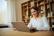 © bnenin - Smiling young woman using laptop at home, portrait.