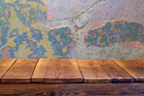 Fototapeta  - Pusty blat drewnianego stołu zbitego ze starych desek, w tle obdrapana wielokolorowa ściana, pomalowana farbą kredową.