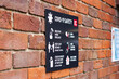 COVID 19 safety information sign for shoppers mounted on brick wall leading to town centre shopping area with shallow depth of field