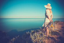 Beautiful Young Woman In A Hat On A High Sea Cliff With A Bouquet Of Flowers In A Retro Hat.