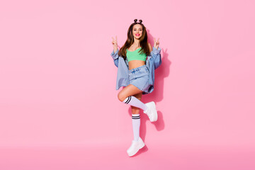 Sticker - Full length photo of pretty funky lady jumping high up showing v-sign symbols wear denim jacket green crop top naked belly skirt knee socks shoes isolated pastel pink color background