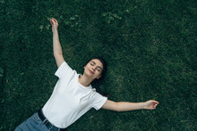 Caucasian Girl 20-25 Years Old Lies On The Green Grass On A Summer Day Smiling, Arms Outstretched, Hugging Everyone. View From Above. View From The Corner. The Concept Of A Happy Life, Vacation