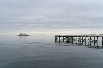 A view of the long pier and the Long Island Sound at Calf Pasture Beach in Norwalk, Connecticut USA on a cold and grey December day. The flat light lends a dreamy feel to the scene.