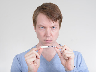 Portrait of young man looking serious while holding cigarette with STOP sign