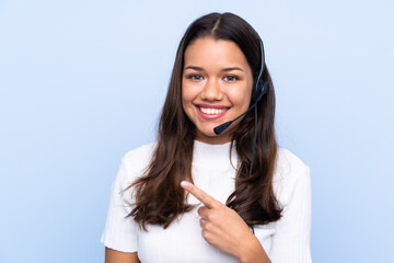 Young telemarketer Colombian woman over isolated blue background pointing finger to the side