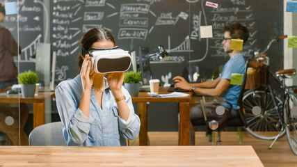 Wall Mural - young female creative developer wearing virtual reality headset works on a laptop, she develops new 