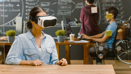 Wall Mural - young female creative developer wearing virtual reality headset works on a laptop, she develops new 
