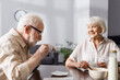 © LIGHTFIELD STUDIOS - Selective focus of smiling senior woman looking at husband drinking coffee at home