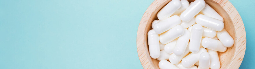 White capsules in wooden bowl on blue background.