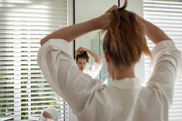 Wall Mural - Woman tying her hair while looking in the mirror