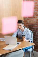 Wall Mural - selective focus of businesswoman using laptop and holding paper cup