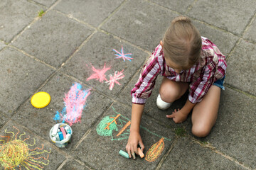 european girl in checkered clothes draws with colorful chalk on the pavement. children's games.