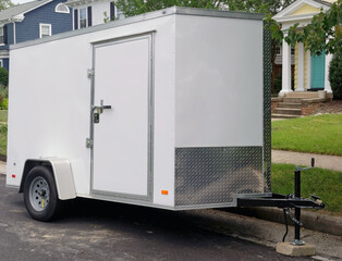 White utility trailer front and side view parked on residential neighborhood street.