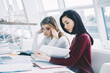 © BullRun - Tired blonde student from exam preparation sitting with friend and searching information in science book sitting in university interior.Young women collaborating on homework in coworking space
