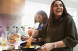 © Sam Edwards/Caia Image - Happy Indian women cooking food in kitchen