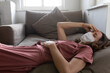 © Wavebreak Media - Woman wearing face mask with headache sleeping on the couch at home