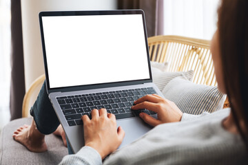 Mockup image of a woman working and typing on laptop computer with blank screen while sitting on a sofa at home