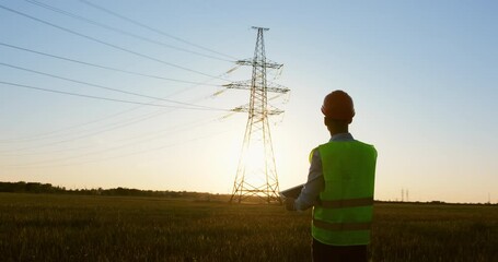 Wall Mural - a power engineer in special clothes holds a tablet in his hands on the background of a high-voltage 