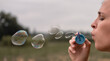© Ekaterina - The girl blows soap bubbles. A young woman sits in nature and blows soap balls. Face in profile.