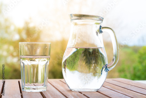 jug with water and a glass on a wooden table on the nature in the garden