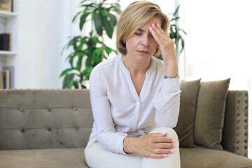 Unhappy middle aged woman sitting on a sofa in the living room.