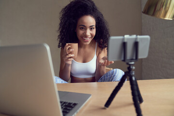 Cheerful curly lady making video call with gadgets