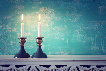 two shabbat candlesticks with burning candles over wooden table