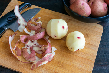 Wall Mural - Peeling Red Potatoes on a Bamboo Cutting Board: Raw potatoes with a vegetable peeler and kitchen knife on a wood cutting board