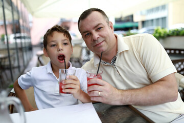 Father and son drinking juice on terrace