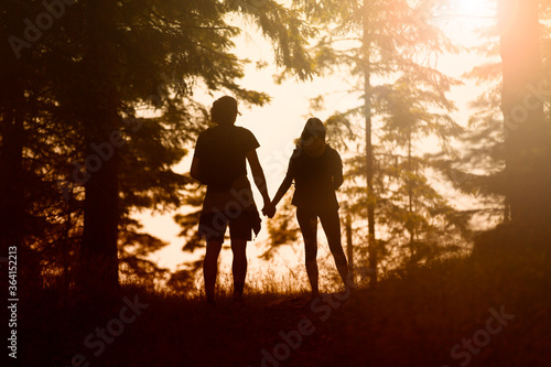 Fotografía Young couple silhouette holdings hands together in the sunny nature