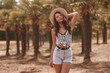 © Dmitry Tsvetkov - Young beautiful woman wearing shorts, shirt and salty hat walking in palms. Tropical resort. Pretty caucasian stylish female model. Life style. Outdoor portrait