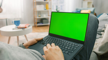 Man at Home Laying on a Couch Using with Green Mock-up Screen Laptop Computer. Guy Using Laptop Device, Browsing Internet, Watching Content, Videos.