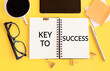 © Nastassia - The text, the word Key To Success, is written in a notebook lying on a yellow table with a pen, coffee, glasses, sticks. Business concept