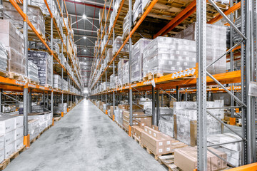 Large industrial warehouse. Tall racks are completely filled with boxes and containers.