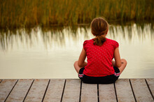 Girl Sitting Alone On Dock Facing Marsh Reeds