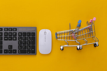 Online supermarket. PC keyboard and shopping trolley on yellow background. Top view